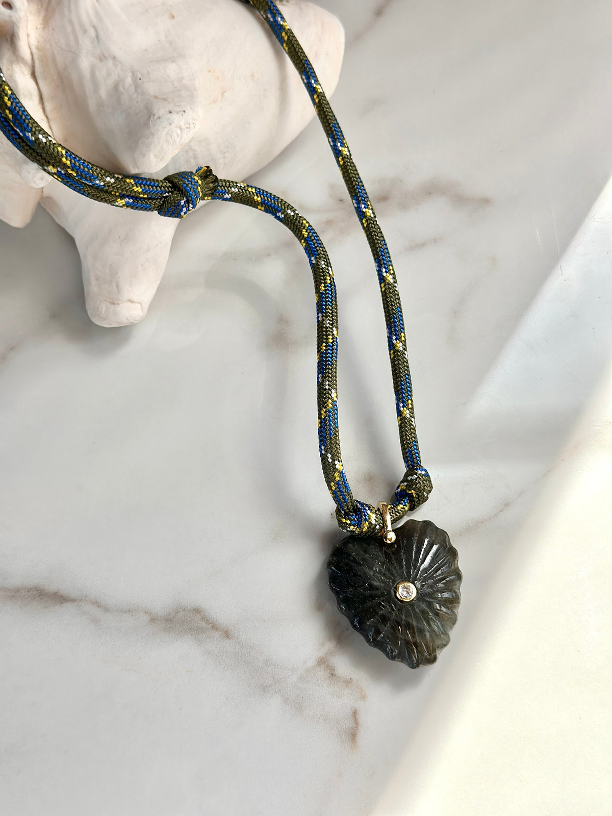 Olive and blue paracord statement necklace with carved dark green stone pendant styled with a seashell.