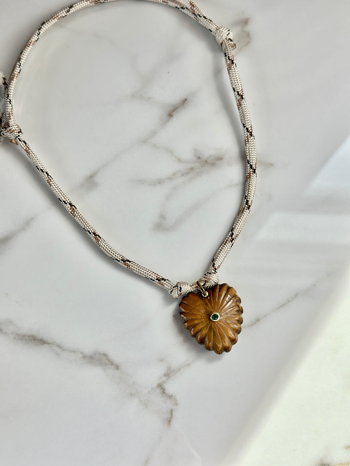 Amber carved stone pendant necklace with cream patterned cord styled with a seashell.
