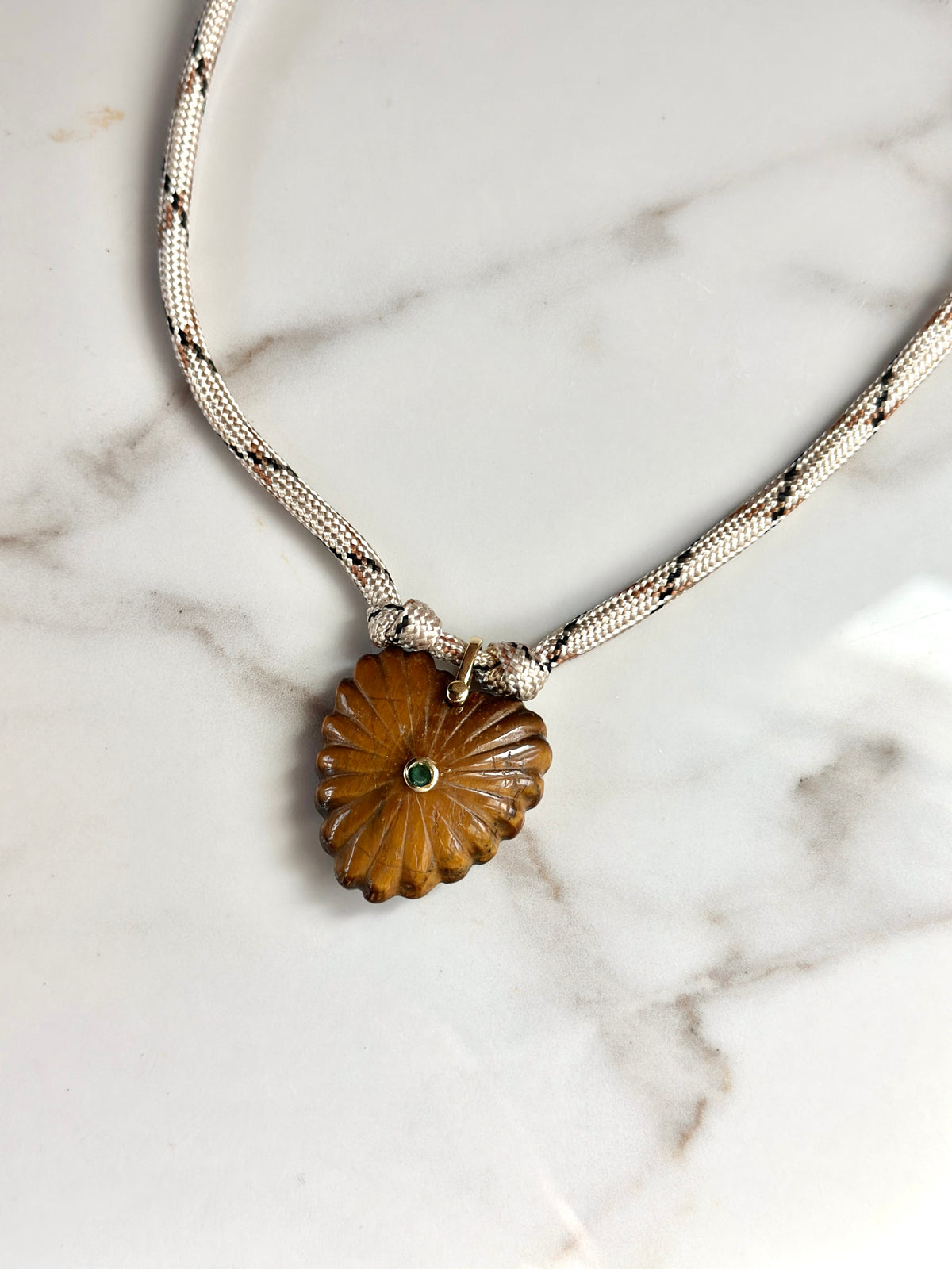 Detailed view of amber carved stone pendant with green CZ accent and cream woven paracord necklace.