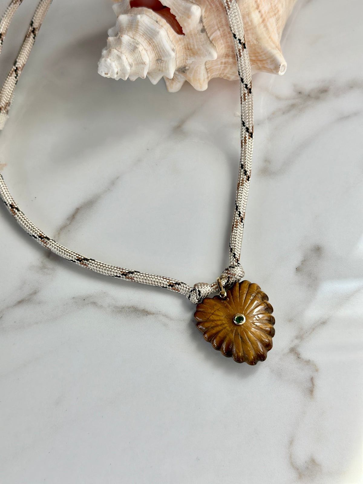 Cream patterned paracord necklace with carved amber stone pendant and green CZ center detail.