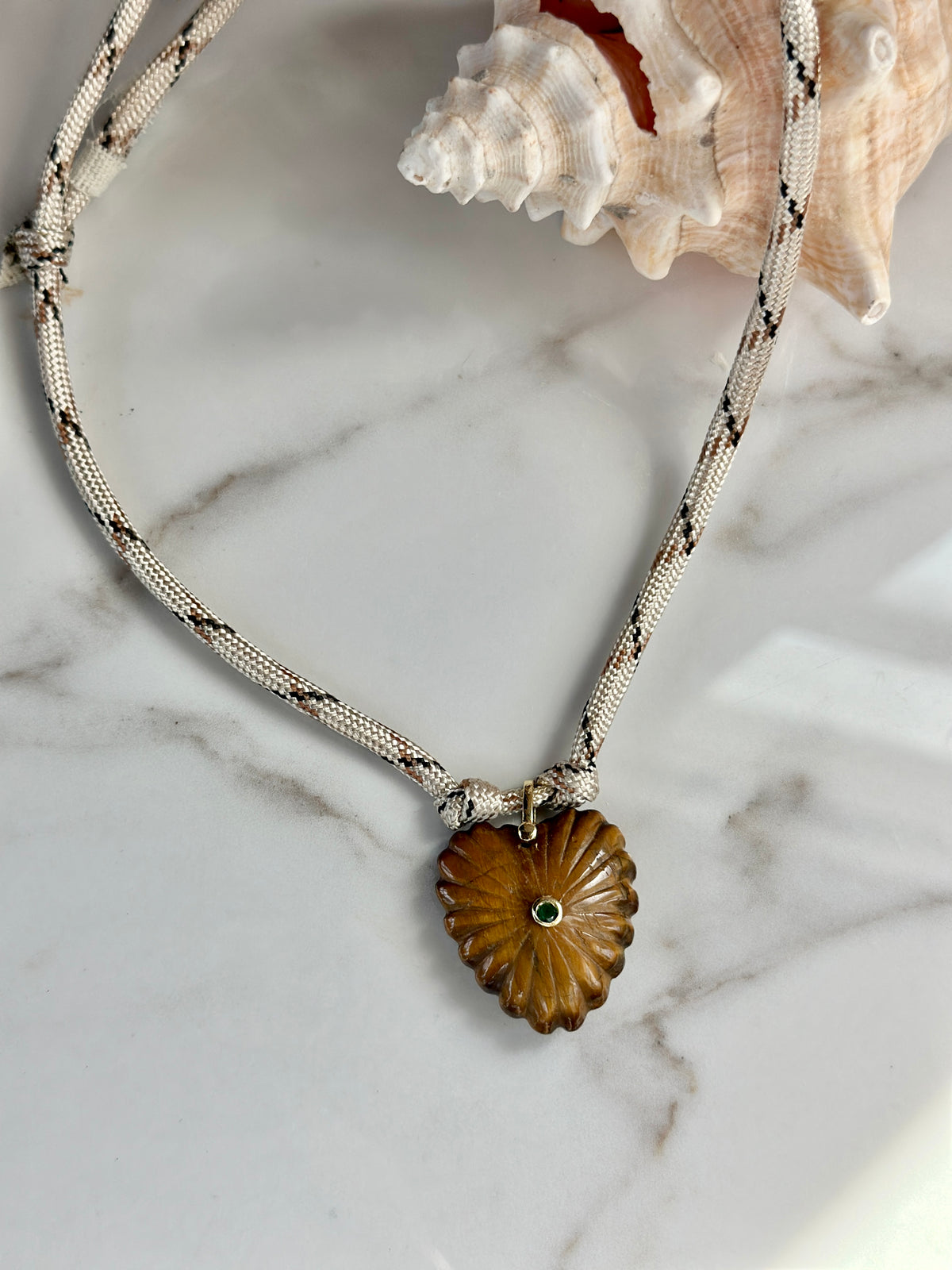 Close-up of carved amber stone pendant necklace with green CZ accent on a cream patterned paracord cord.