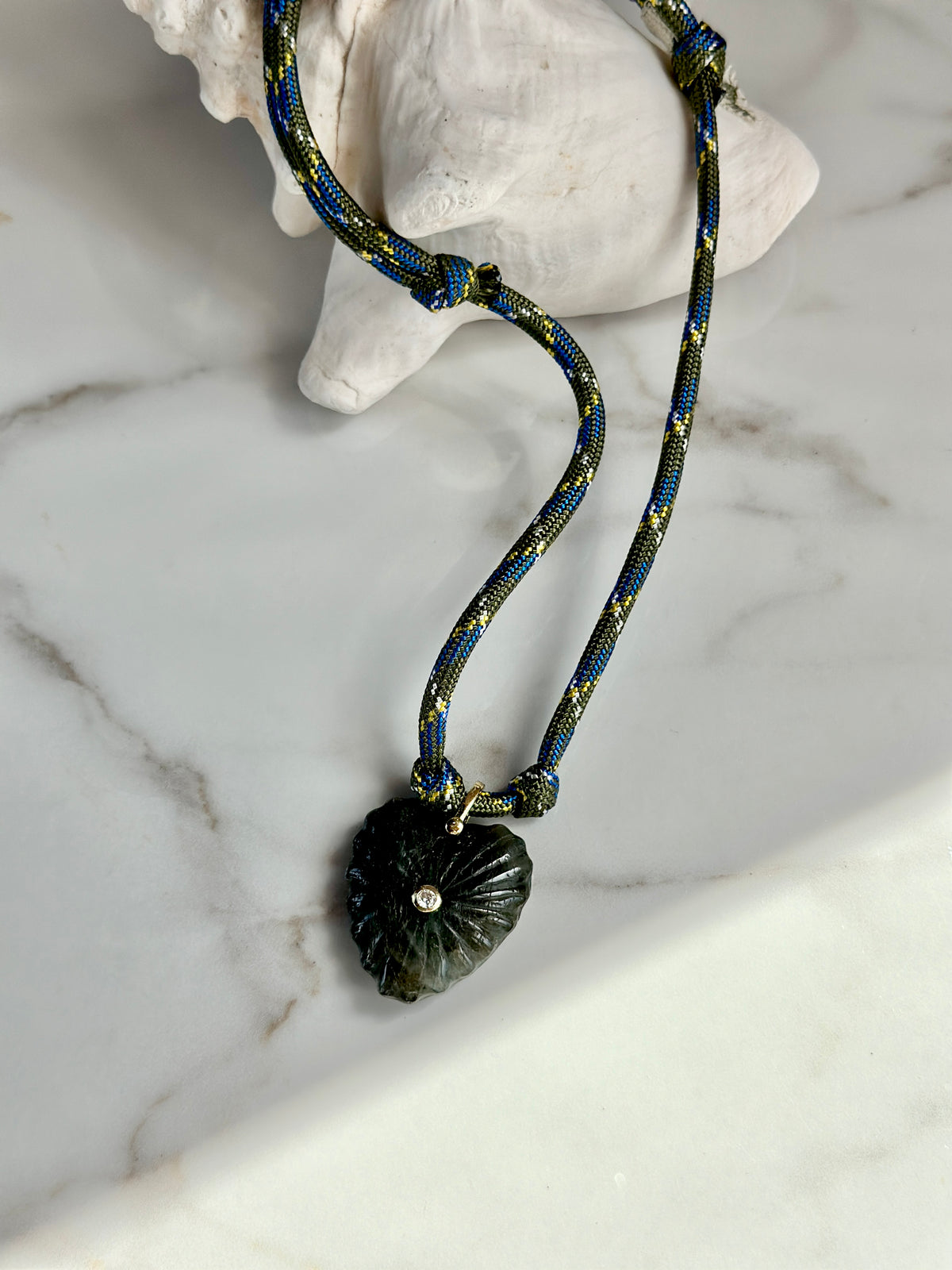 Close-up of dark green carved stone pendant with sparkling CZ accent on an olive and blue paracord necklace.