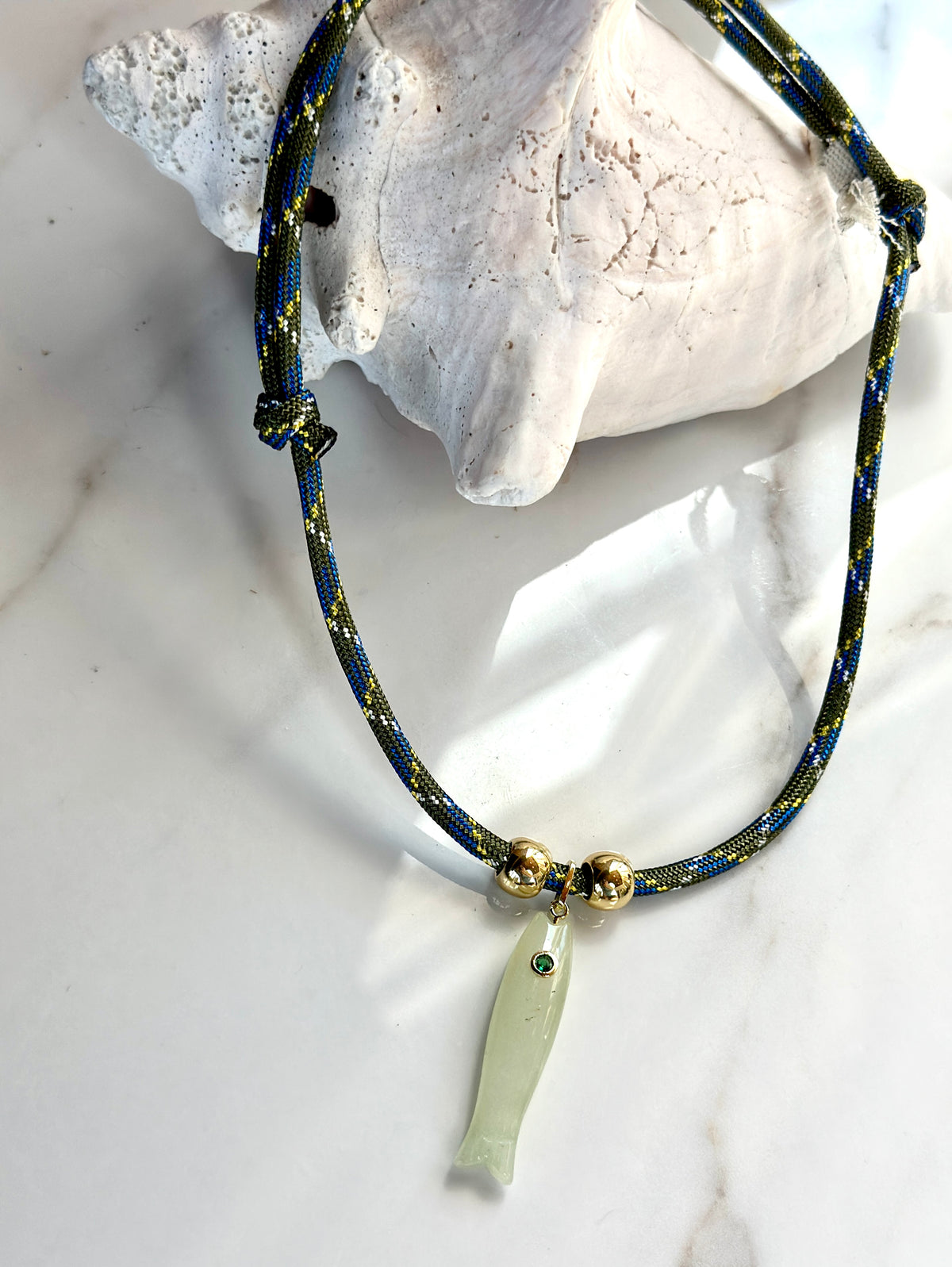 Natural gemstone fish necklace featuring a green jade pendant with CZ eye on an olive blue patterned cord.

