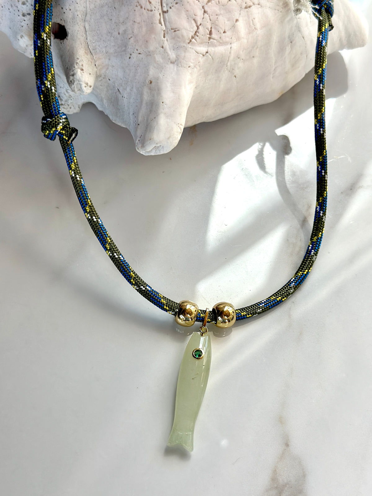 Adjustable cord necklace with natural green jade fish pendant and gold-tone bead accents styled with a seashell.
