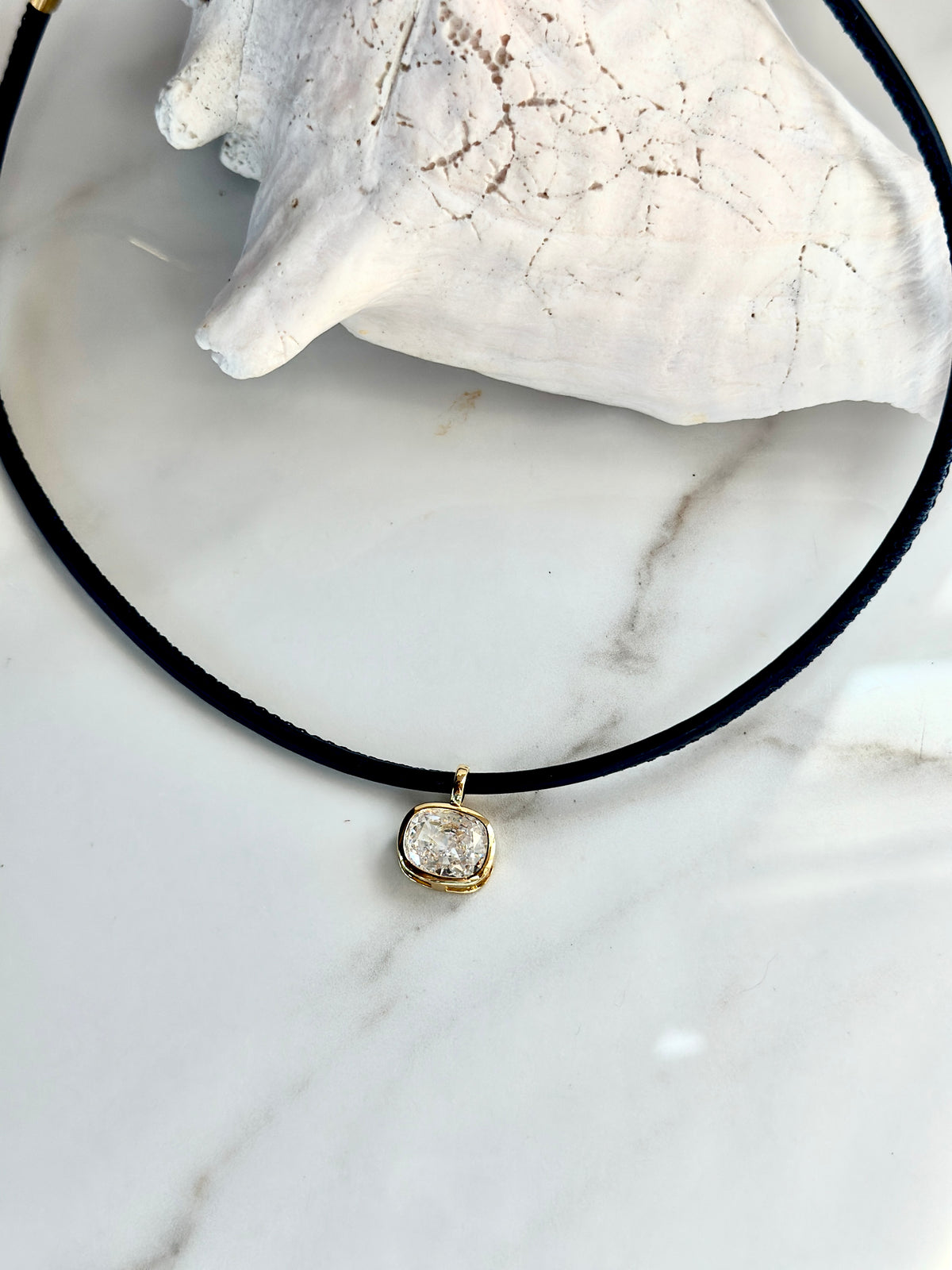 Close-up of navy cord necklace with cushion-cut cubic zirconia pendant framed in gold.
