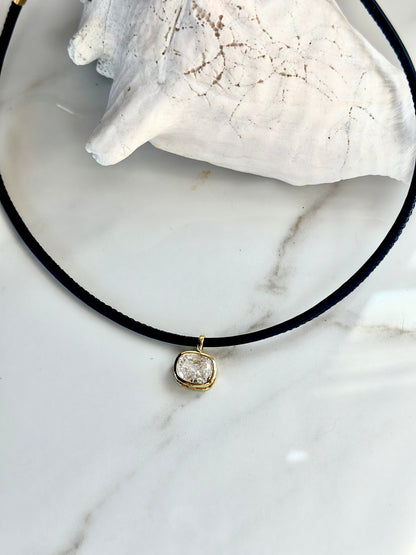 Close-up of navy cord necklace with cushion-cut cubic zirconia pendant framed in gold.
