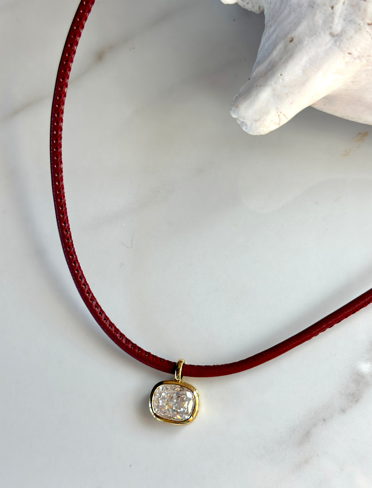 Red cord pendant necklace with sparkling cubic zirconia stone in a gold setting.

