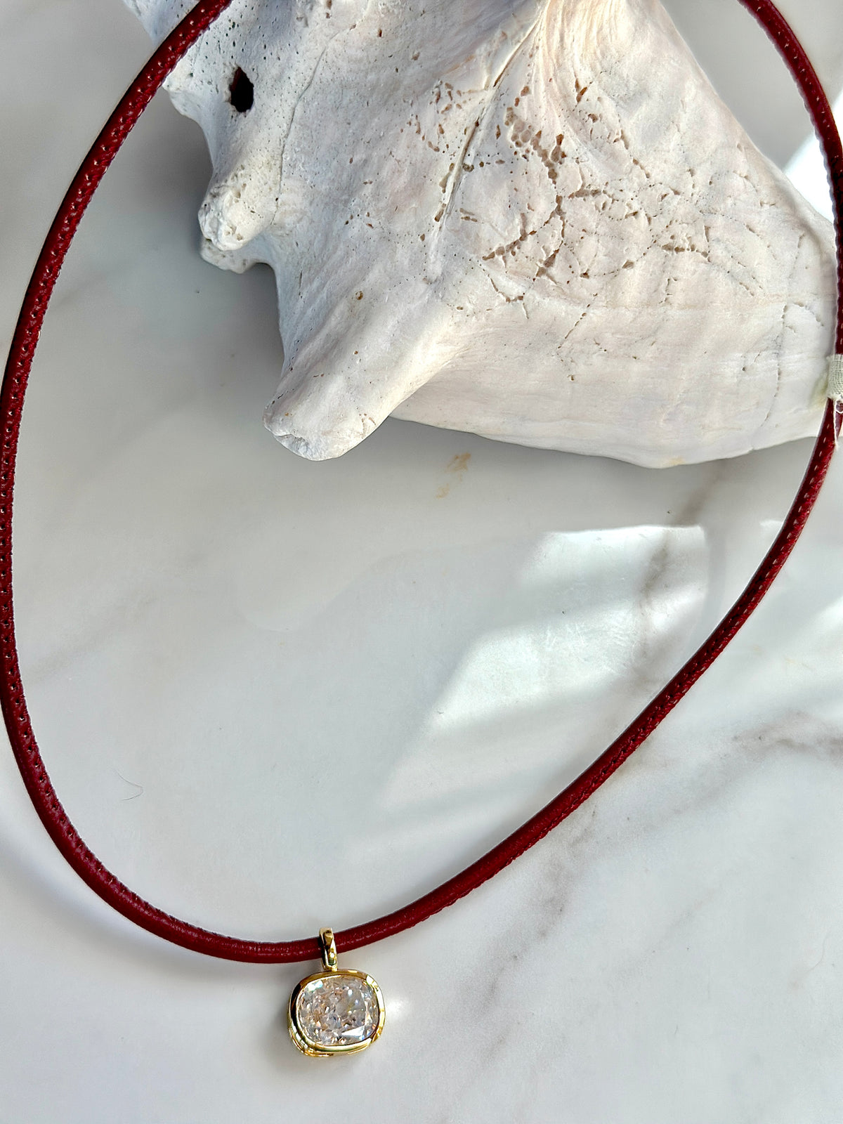 Close-up of red cord necklace with gold-set cushion CZ pendant.
