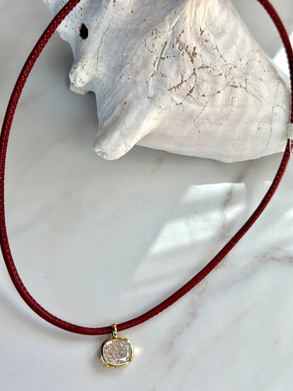 Close-up of red cord necklace with gold-set cushion CZ pendant.
