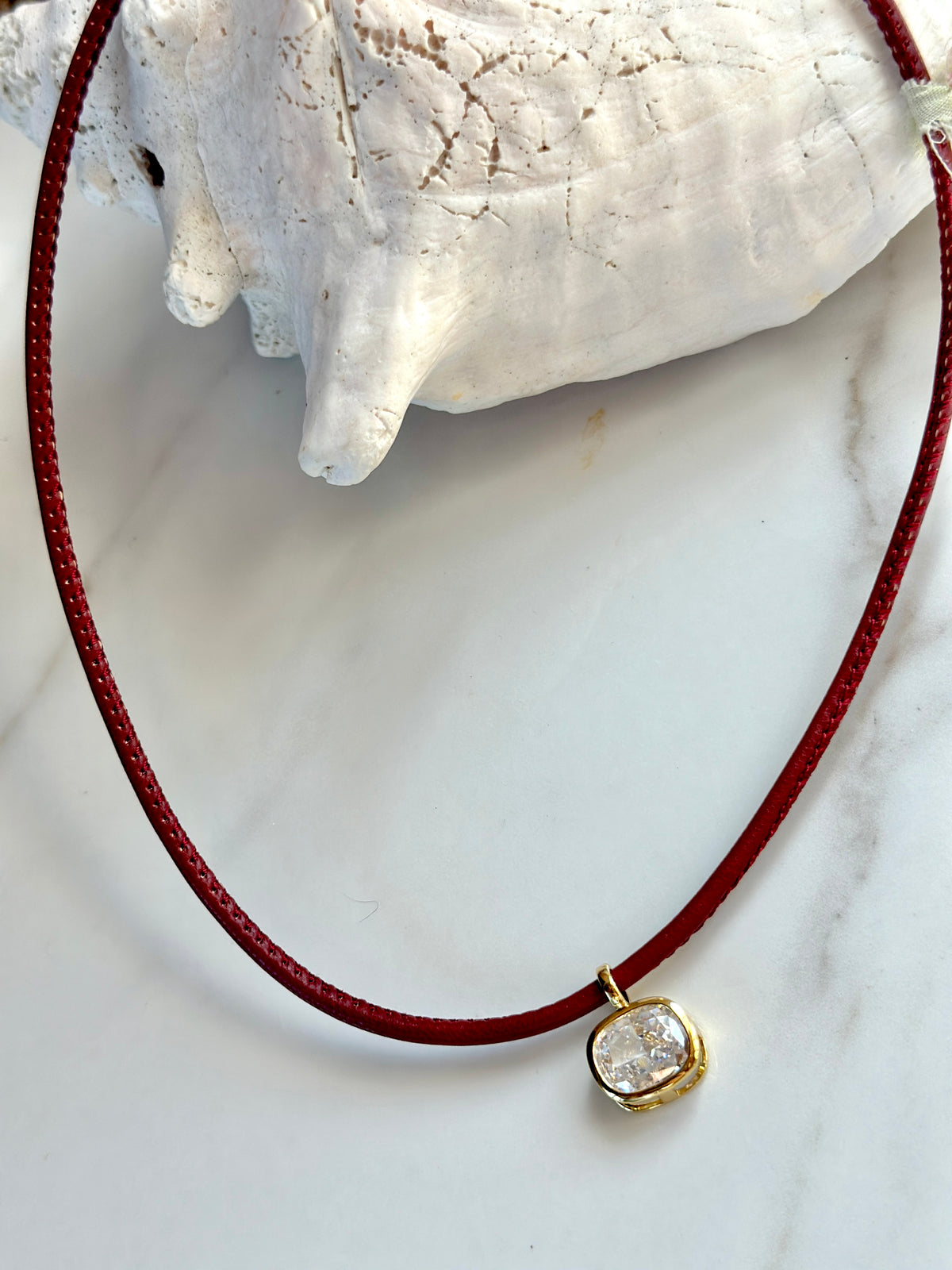 Red cord necklace with sparkling cushion-cut cubic zirconia pendant framed in gold.