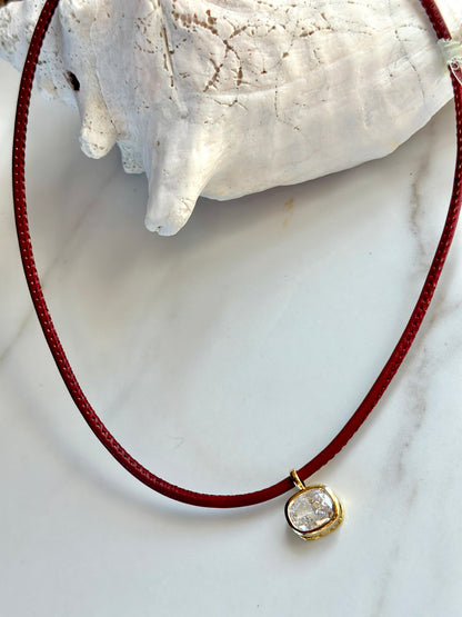 Red cord necklace with sparkling cushion-cut cubic zirconia pendant framed in gold.