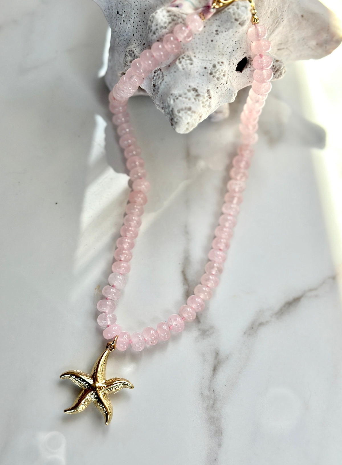 Coastal pink gemstone necklace with gold starfish pendant styled with white coral.
