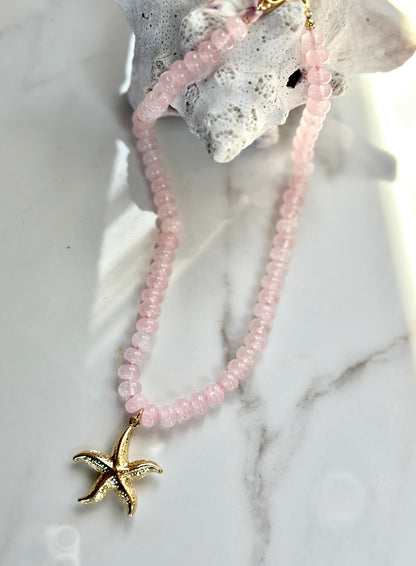Coastal pink gemstone necklace with gold starfish pendant styled with white coral.
