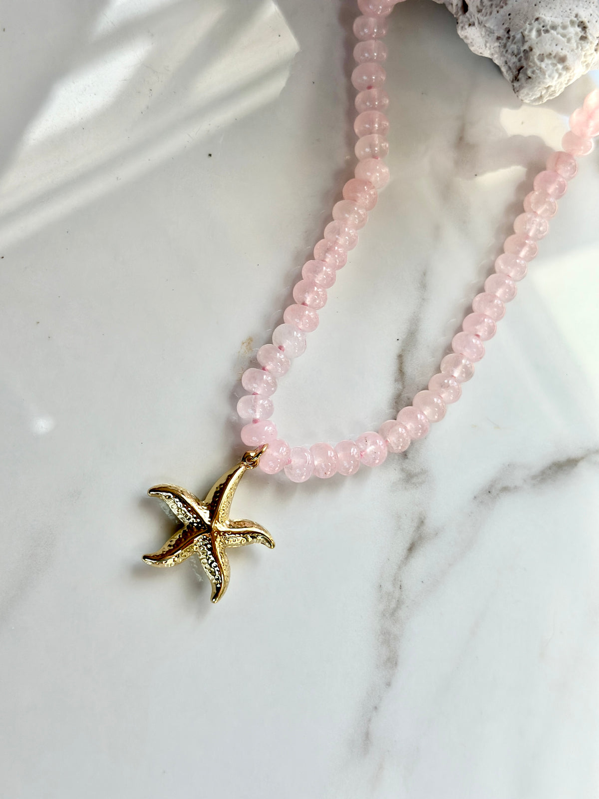 Pink and gold natural gemstone necklace featuring a textured starfish pendant.

