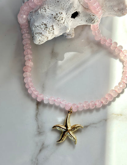 Pink natural gemstone necklace with gold starfish pendant styled over white coral.
