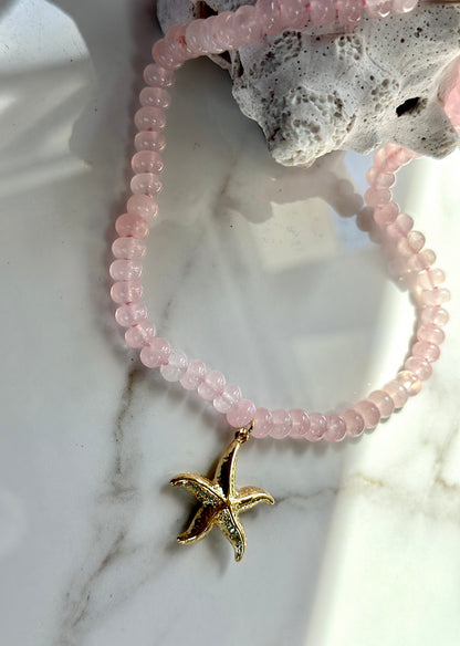 Close-up of pink natural gemstone beads and textured gold starfish pendant.
