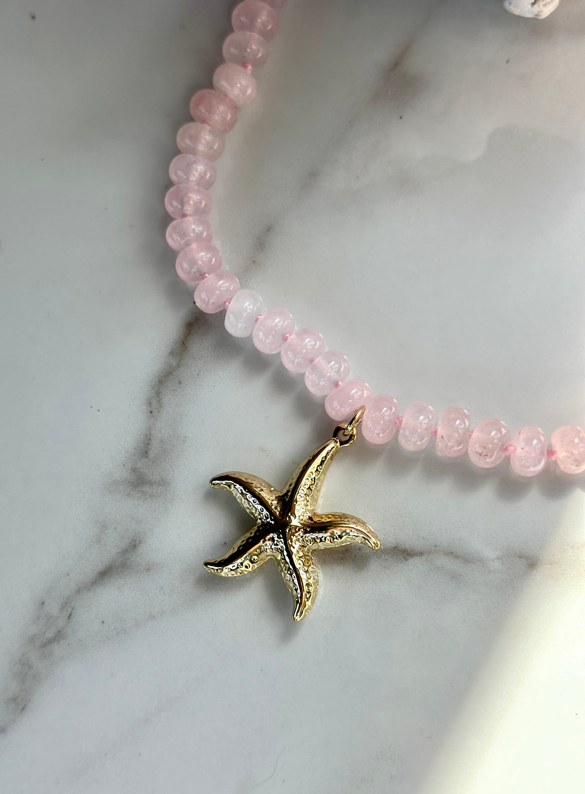 Close-up of textured gold starfish pendant on a pink natural gemstone necklace.