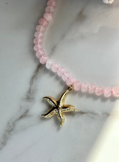 Close-up of textured gold starfish pendant on a pink natural gemstone necklace.