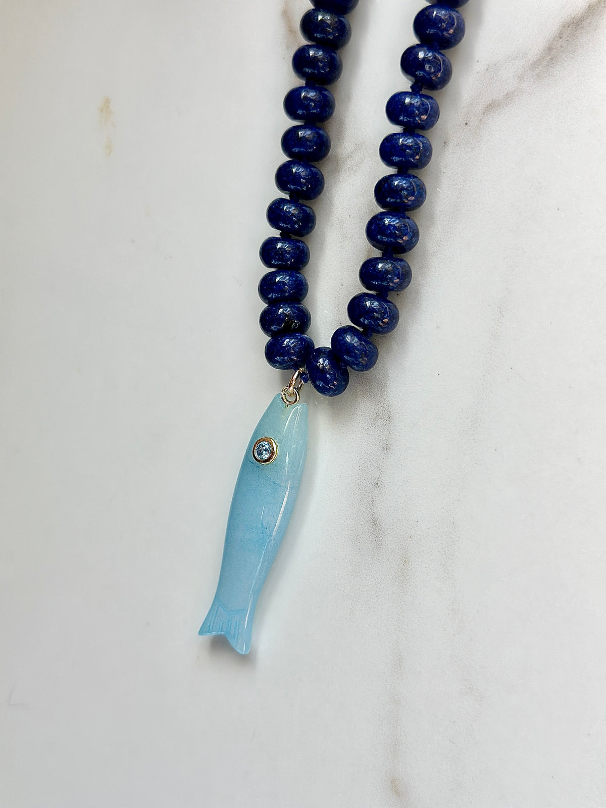 Blue gemstone beaded necklace with light blue carved fish pendant and gold detailing
