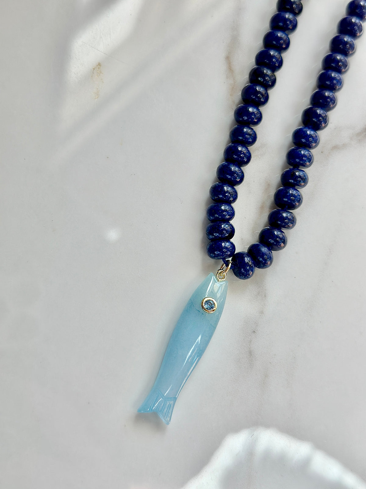 Light blue gemstone fish pendant on deep blue beaded gemstone necklace
