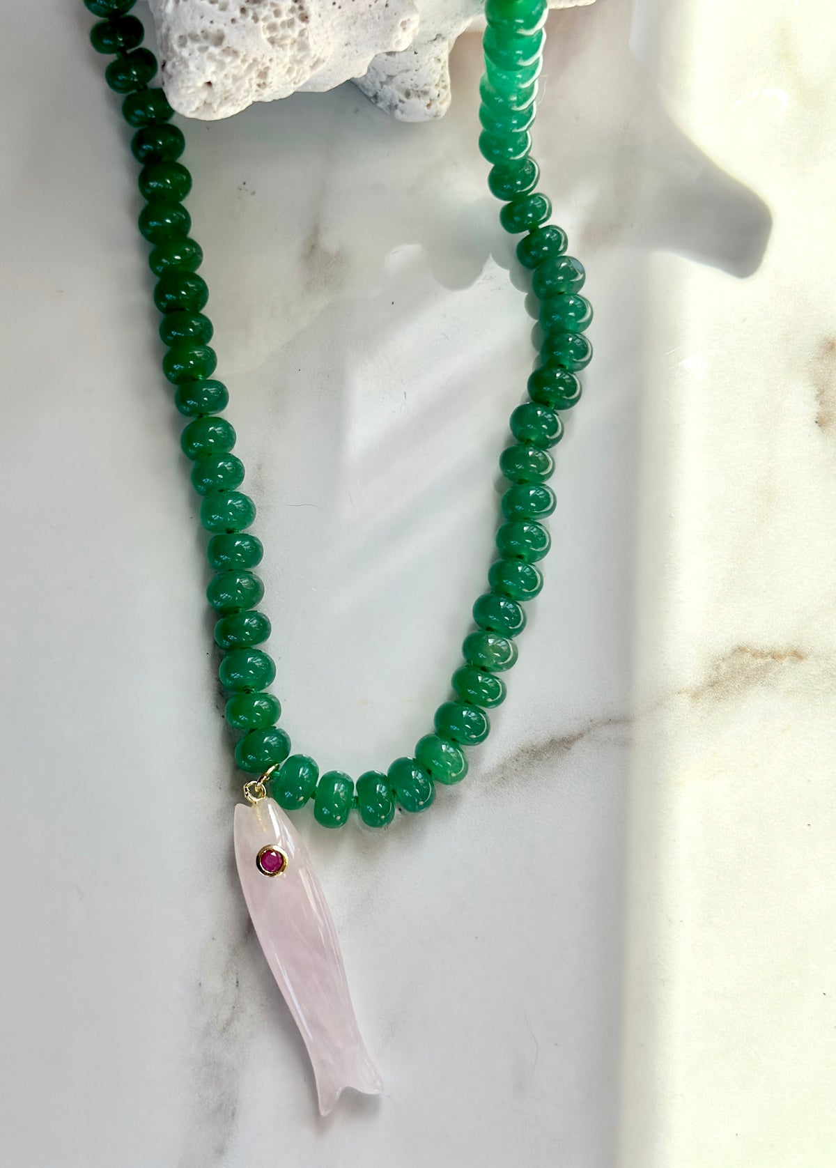 Green beaded gemstone necklace with pale pink fish pendant and gemstone accent.