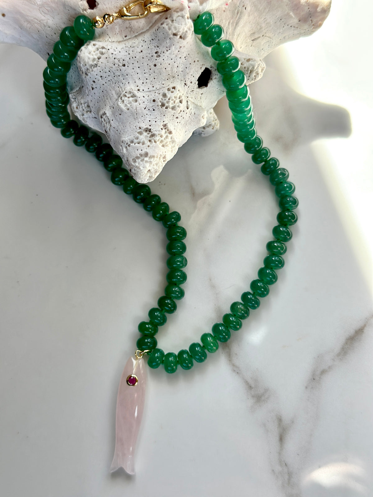 Green gemstone fish pendant necklace with pink carved fish and gold clasp.