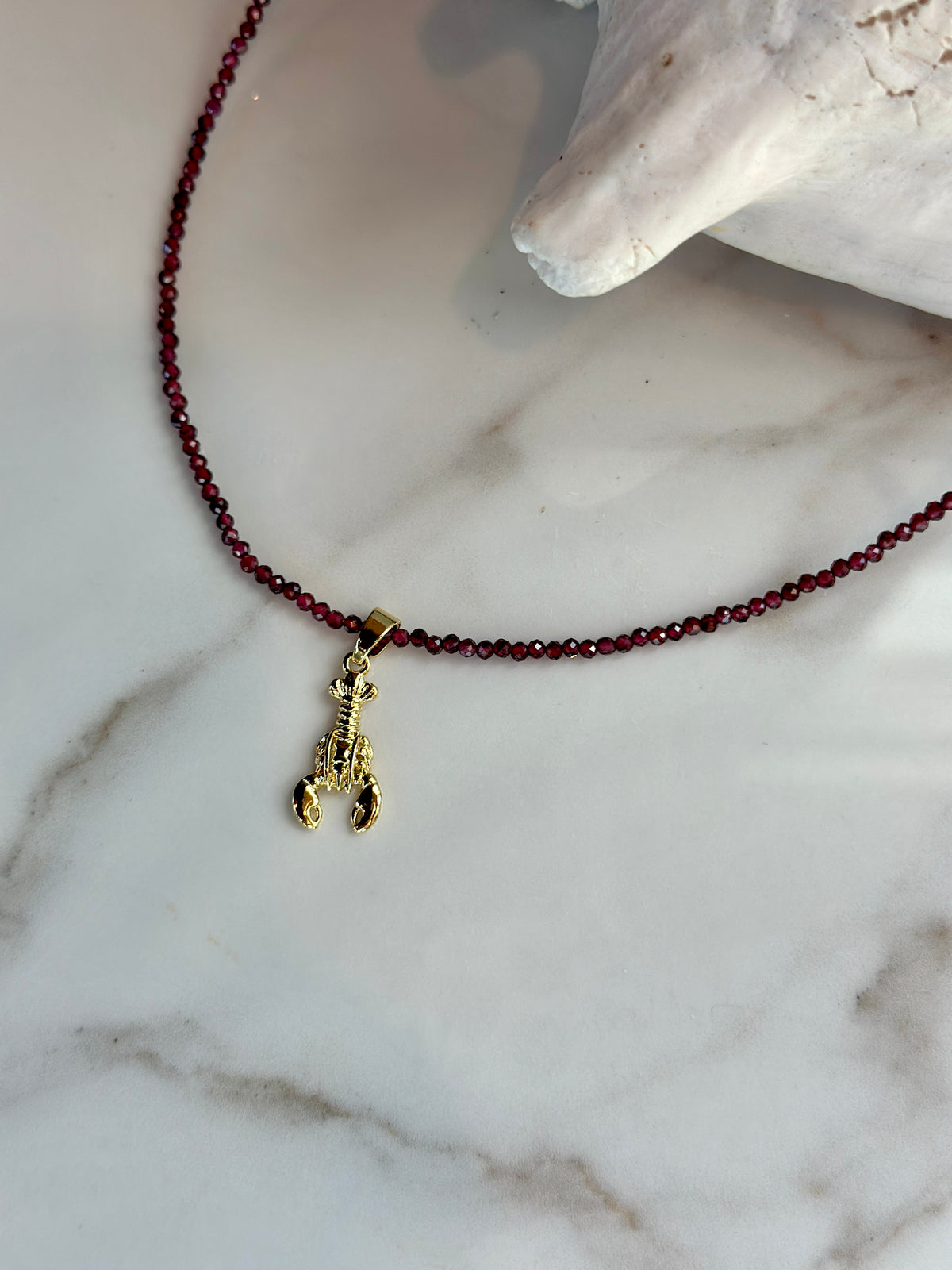 Faceted garnet gemstone bead necklace with a small gold lobster charm.
