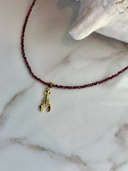 Faceted garnet gemstone bead necklace with a small gold lobster charm.
