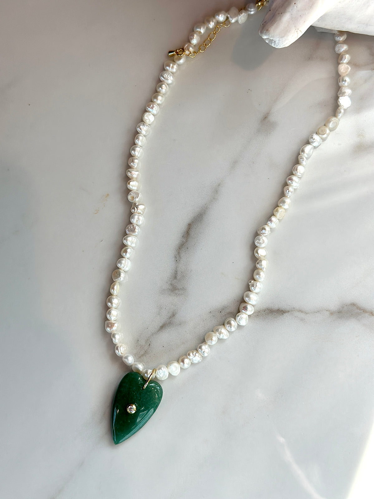 A beaded necklace with irregular white pearls and a polished green teardrop pendant, displayed on a white marble surface.